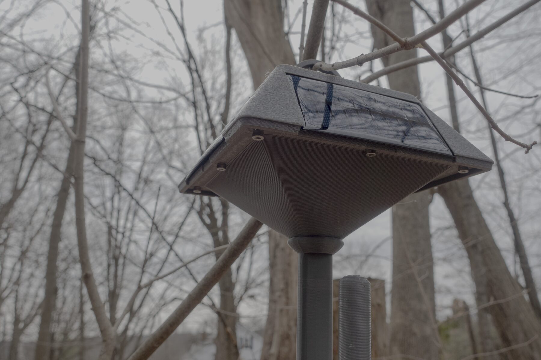 Lantern-style MeshCore repeater installed outdoors with the solar face and hanging body visible in natural field context.